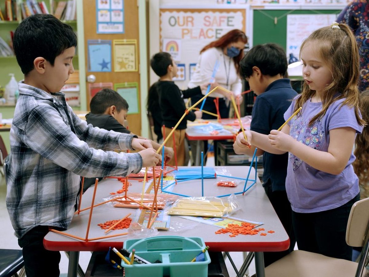 Two kids building straw structures at a table